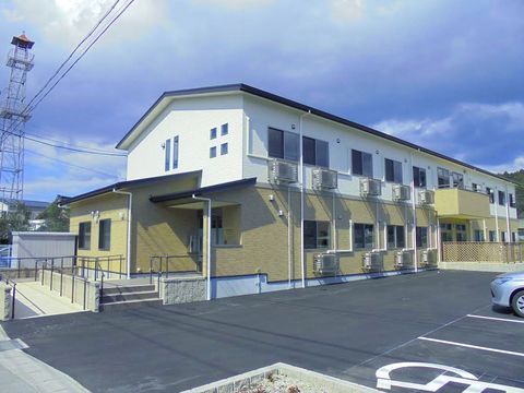 広い駐車場が広がっている向こう側に立っている、二階建ての施設外観