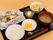 黒いお盆の上にご飯、お味噌汁、たくあん、ホイル焼き、サラダなどが載っている。デザートにはコーヒーゼリーがある。