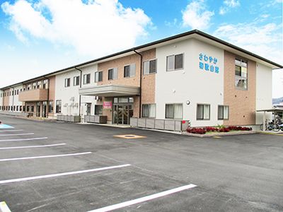 建物前に駐車場が広がっている、白色と黄土色の外壁をした二階建ての施設