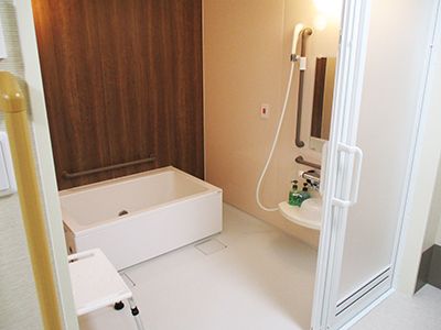 奥には湯船があり、そのそばに木目調の壁がある。壁には手すりが付いており、壁の色と合うように茶色になっている。