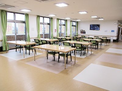 複数のテーブルが等間隔で置かれている。それぞれ椅子が２脚〜４脚用意されている。壁掛けテレビと手すりが設置されている。
