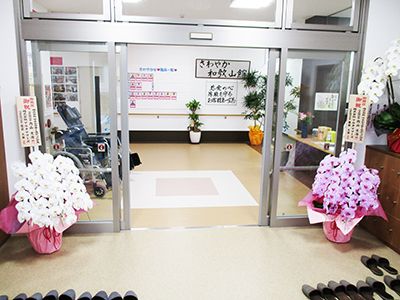 自動ドアの手前にスリッパが多数置かれている。自動ドアを入ると右手に受付があり、左手には車椅子が置かれている。