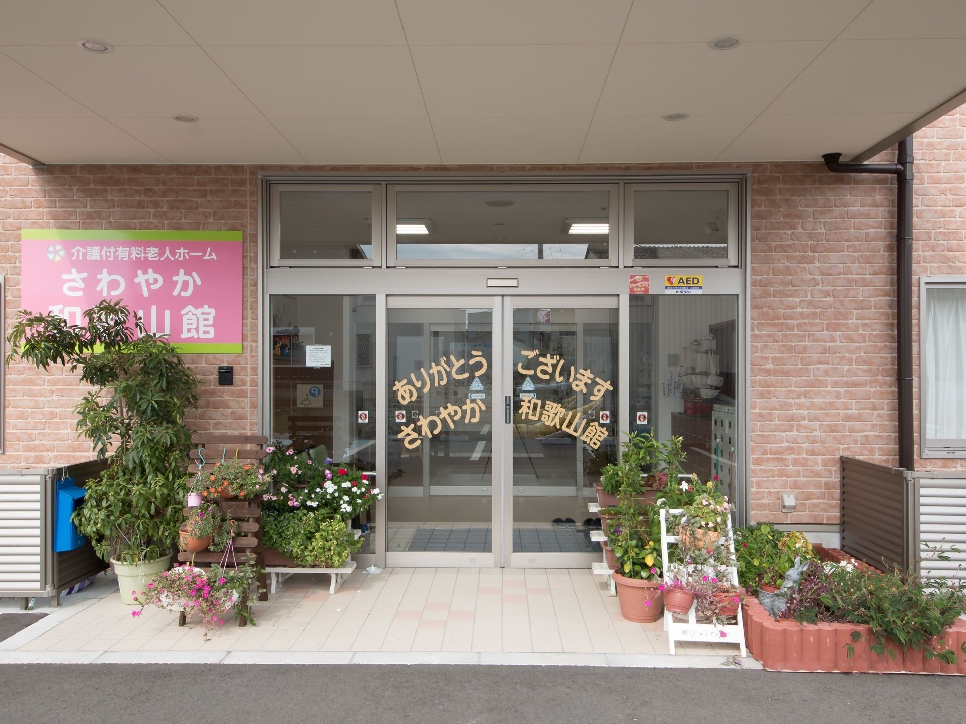 入り口は自動扉になっている。外壁に施設名が記された看板が設けられており、道路から目立ちやすい。入り口には花が飾られている。