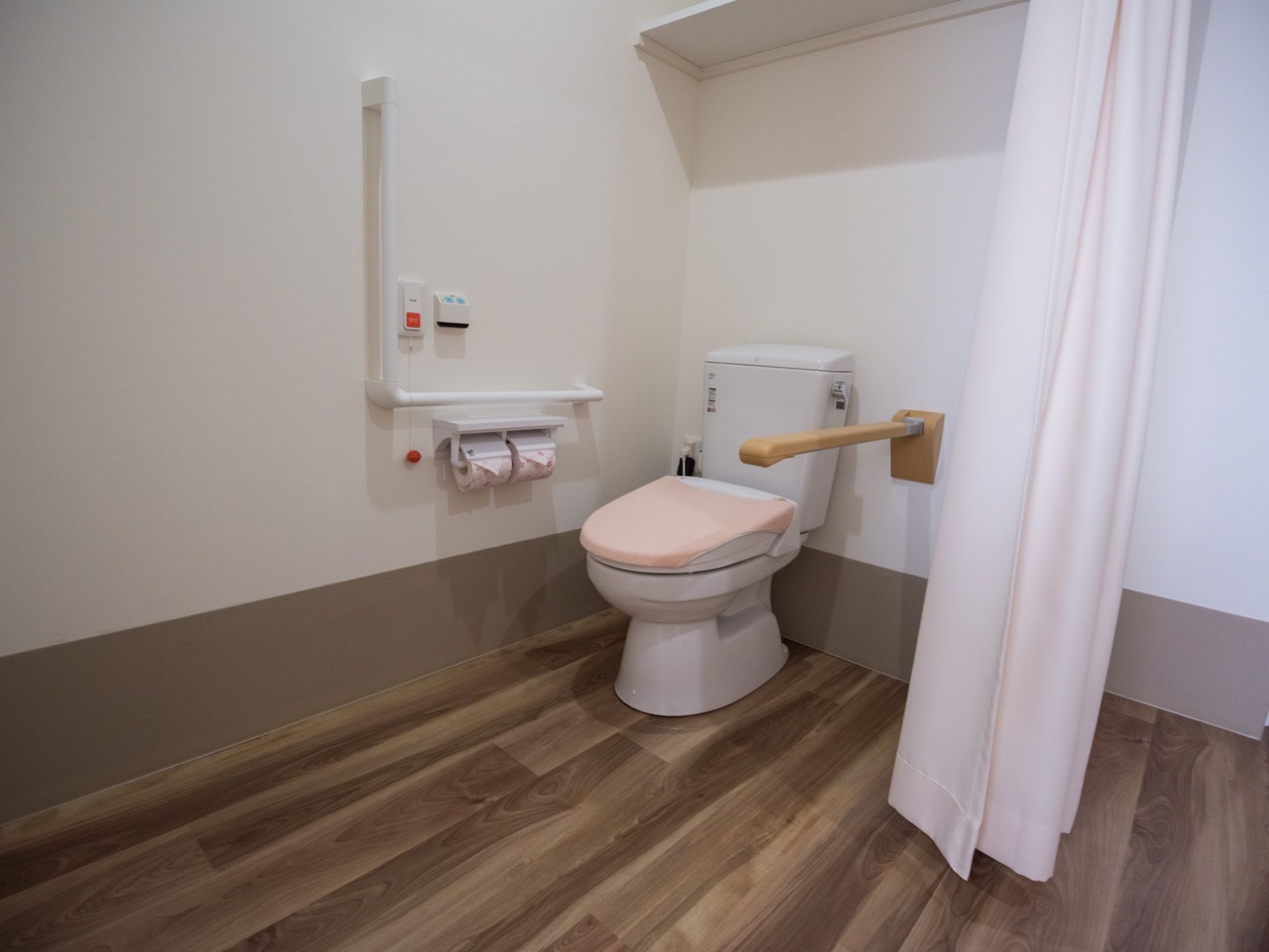 ナースコールが設置されているトイレで、上部に収納棚が設置されている。通路との間は段差のないフローリングとなっている。