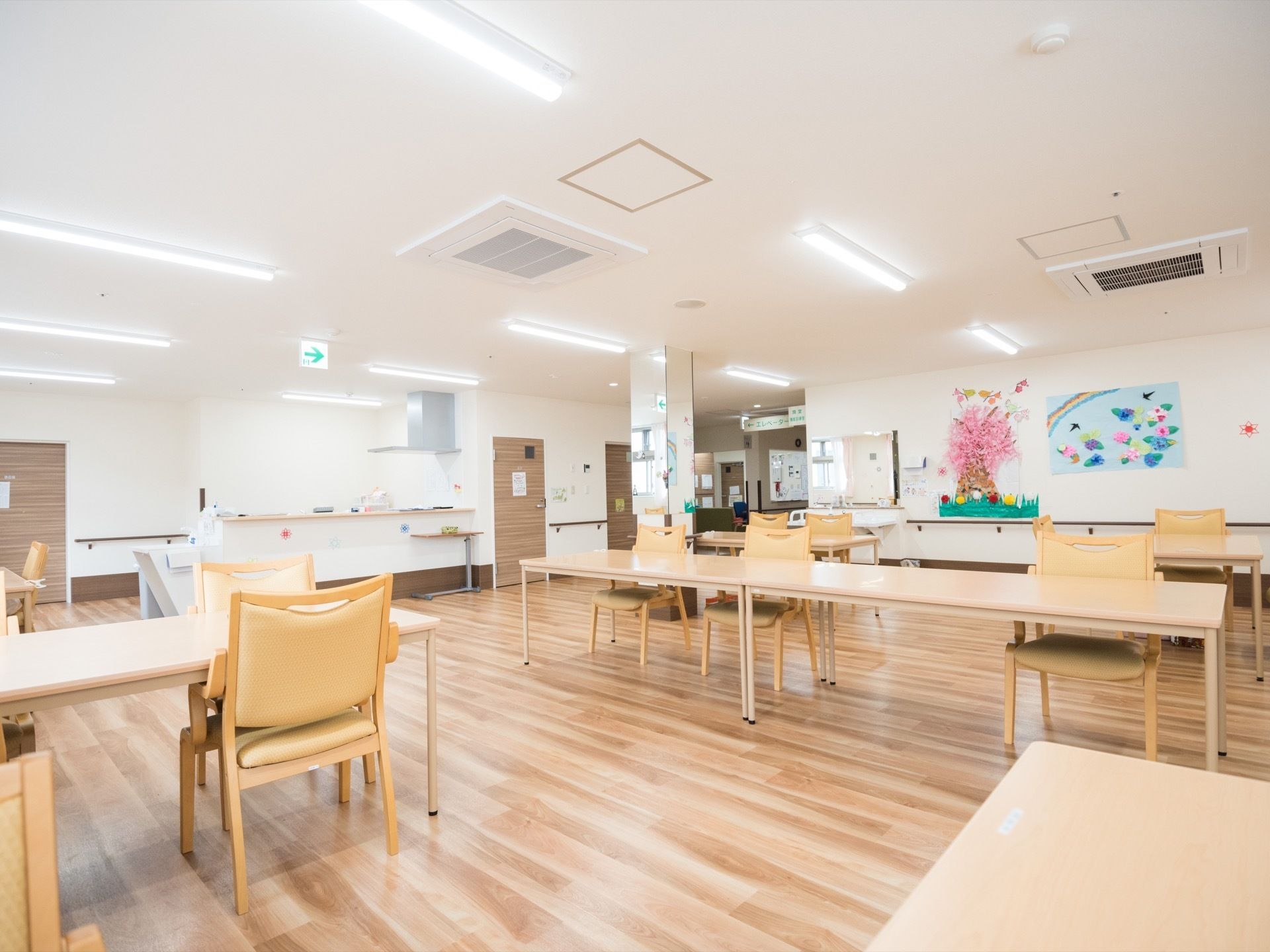 カウンターキッチンと洗面台が設置されている食堂である。フロアには木のぬくもりが感じられる複数のテーブルセットが置かれている。