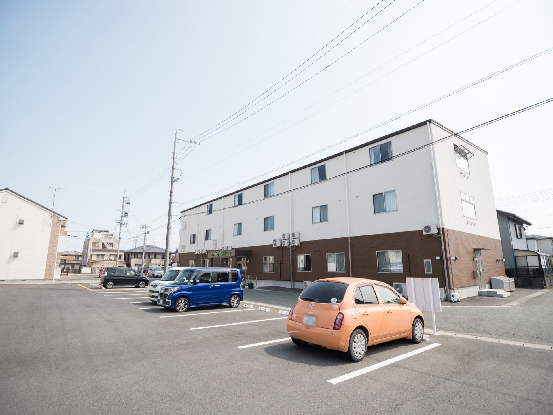 閑静な住宅街の中にある住まいで、道路を挟んで向かい側にはアスファルトで舗装された駐車場が完備されている。