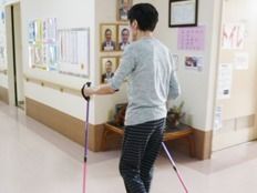 廊下に複数の写真や掲示物が貼られている。入居者様が２本のスティックを持って、ウォーキングのような運動をしている。