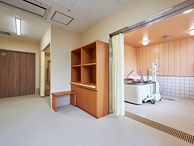 脱衣所に、手すり付きの棚が置かれている。浴室入り口はカーテンが掛けられており、リフト付きの浴槽が設置されている。