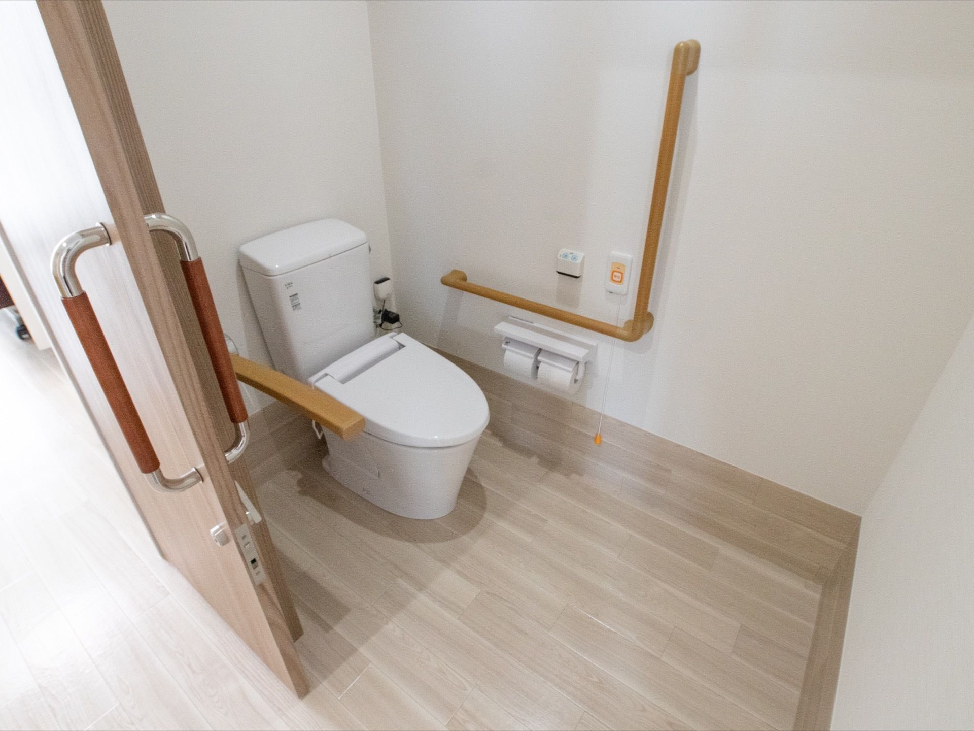 トイレの便座の両側に掴まれる場所を用意している。緊急コールは、ボタンを押すか、床側から紐を引くと作動する仕組みだ。