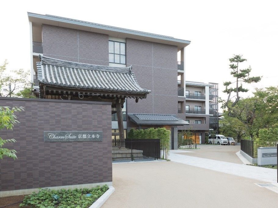 高齢者向けの施設は、お寺の境内に建てられている。広々とした敷地内には駐車スペースがあり、木々が植えられている。