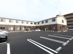 広々とした敷地に建てられている施設の外観。外壁はブラウンとベージュのスッキリしたデザインになっている。敷地内に駐車スペースを完備している。