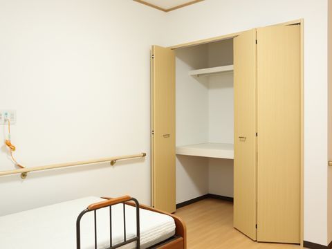 ベッドが一台見える。手すりがある。壁に緊急呼び出しブザーがついている。観音開きのクローゼットが括り付けてある。