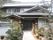 瓦屋根が特徴的な古民家風の２階建てグループホームである。入口は引き戸となっており、玄関前の道の両サイドに鉢植えが並んでいる。