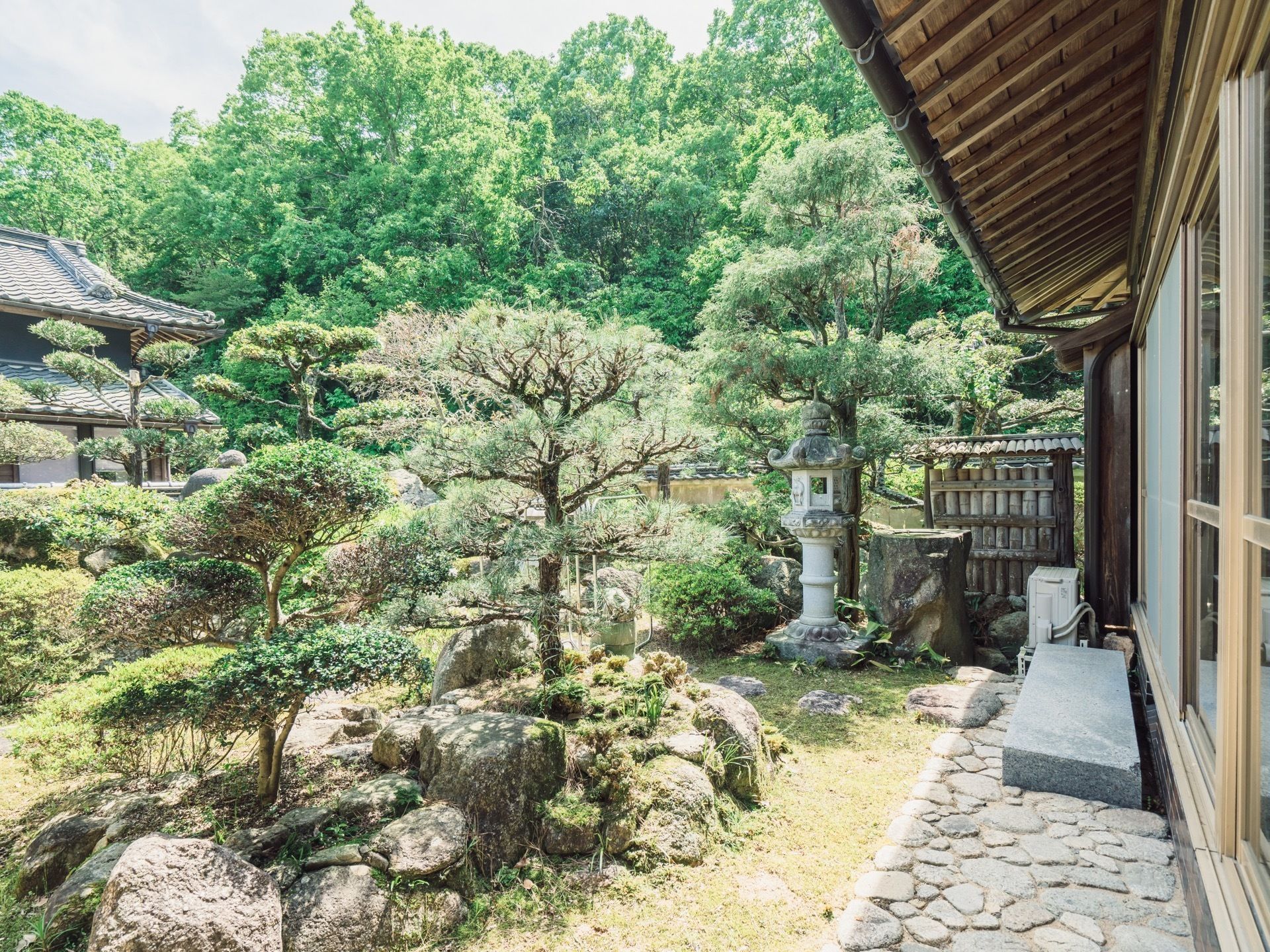 大きな石や庭木を配置した、荘厳な雰囲気の日本庭園である。塀の向こう側にも、高い木々が豊かに茂っている。