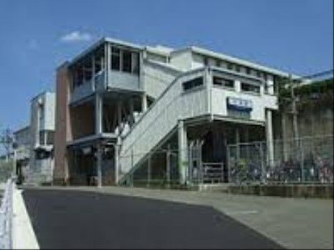 白い外観の駅舎がある。すぐ目の前にはフェンスで囲まれた駐輪場があり、たくさんの自転車が置かれている。
