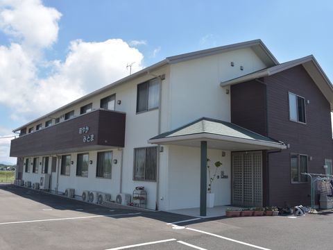 雄大な自然に囲まれた立地環境は建物の周辺もエントランンスの前も広々としている。2階建ての外観は格子戸風の玄関ドアがお洒落感を演出している。