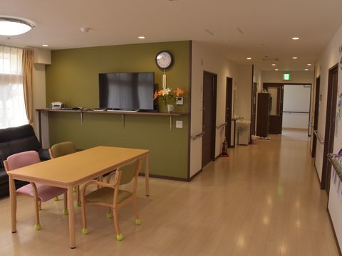 緑色の壁にテレビが置かれ、その前にテーブルセットがある共有スペース