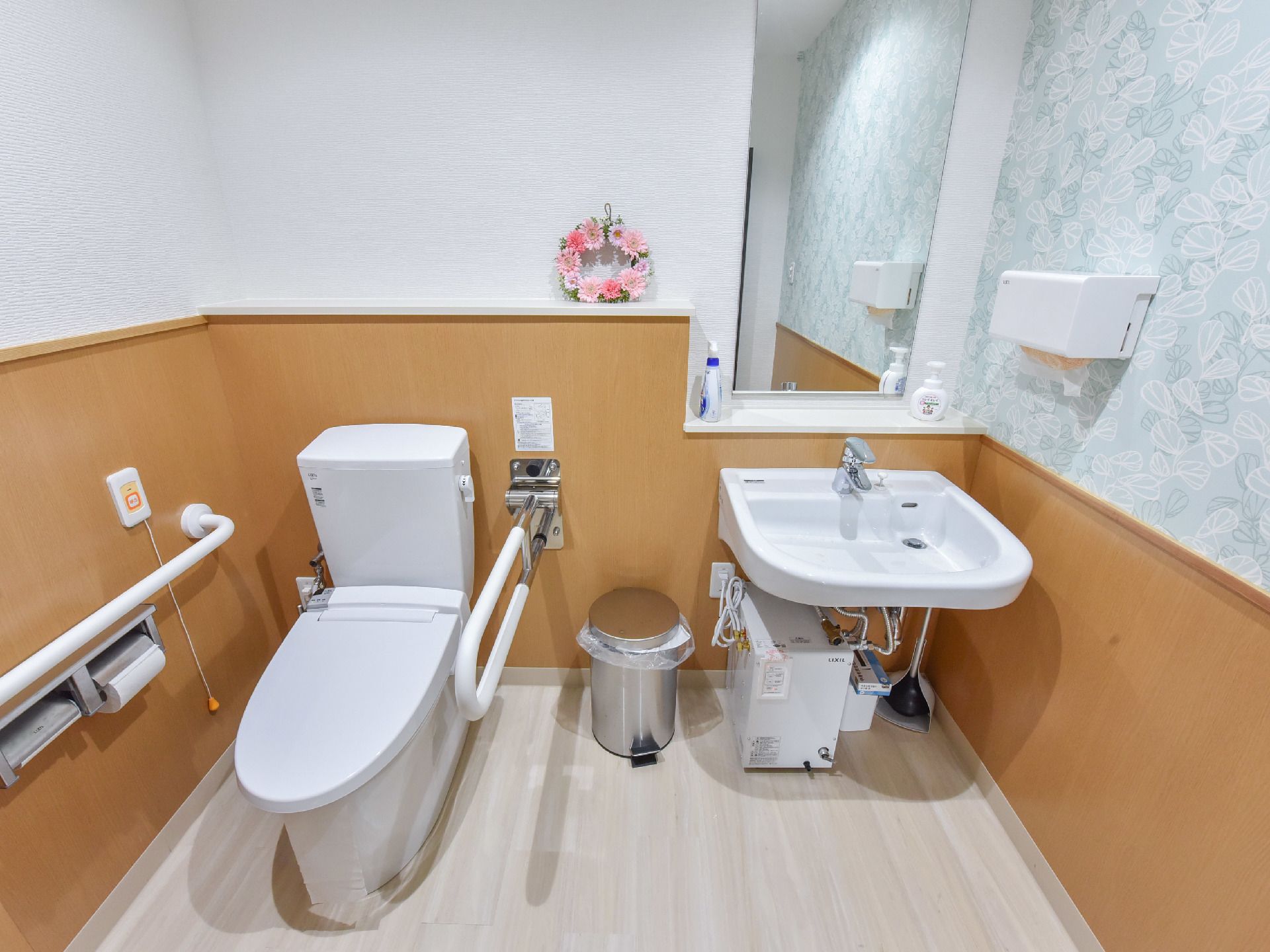 トイレの奥には、様式の便器と洗面台が設置されている。洗面台の前には大きな鏡があり、横にはペーパータオルホルダーがある。