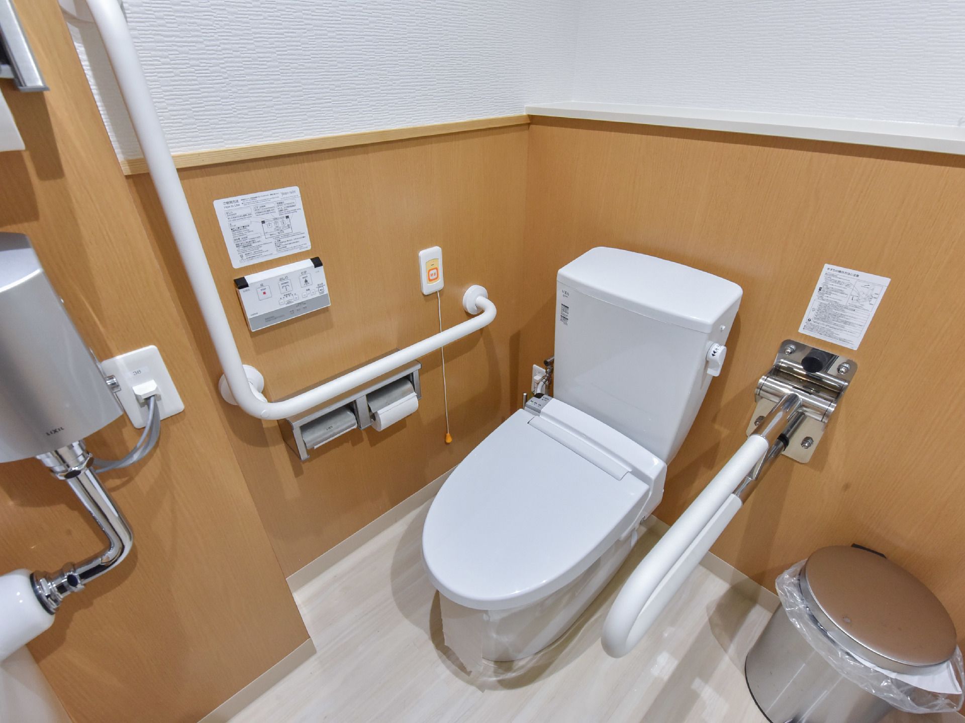 便器の横側には、可動式の手すりがあり、壁側にはL字型の手すりが取り付けられている。非常呼び出しのボタンが壁に設置されている。