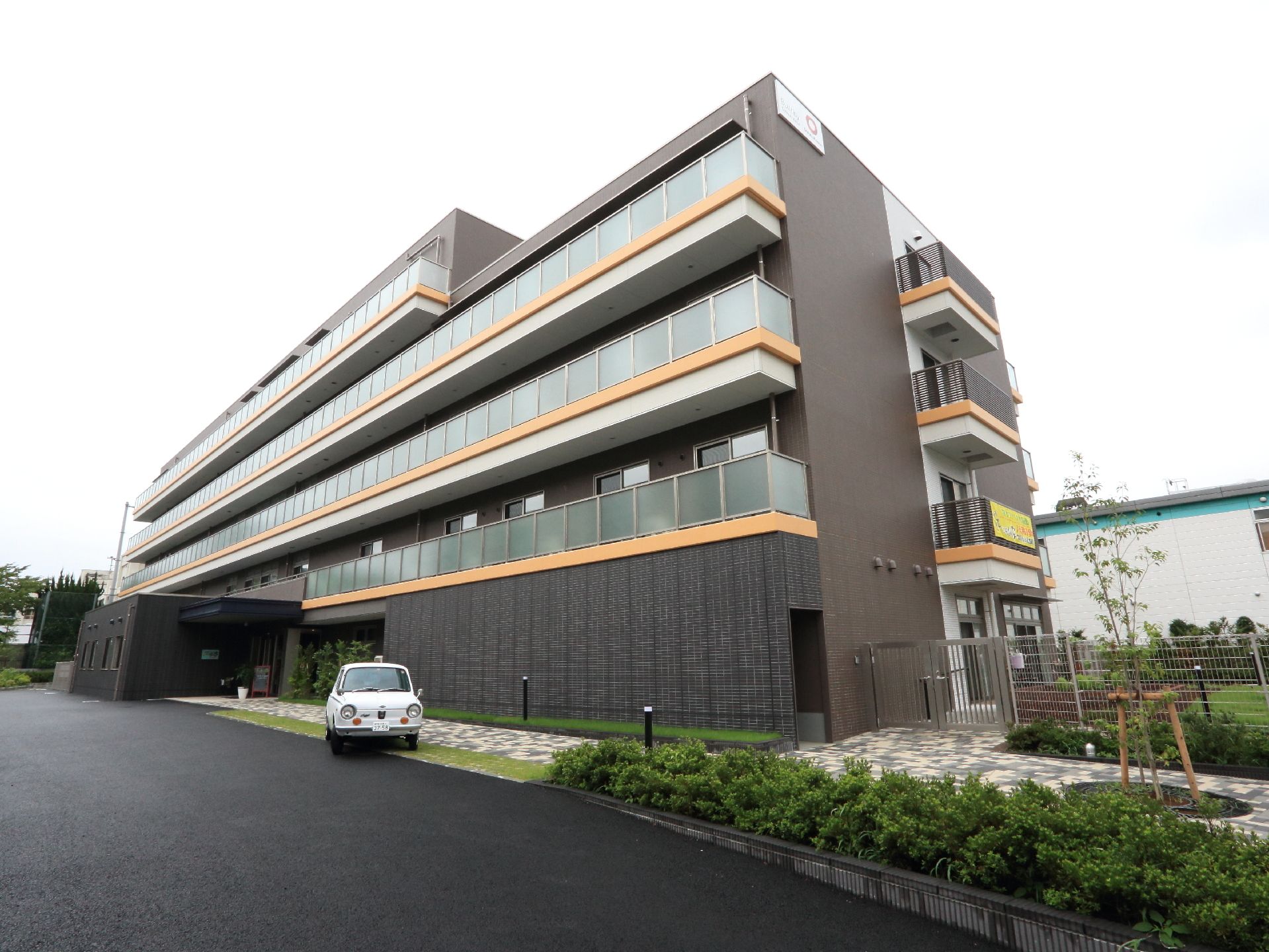 石畳の通路が建物へ向かって続いている、黒い外壁の四階建て施設外観