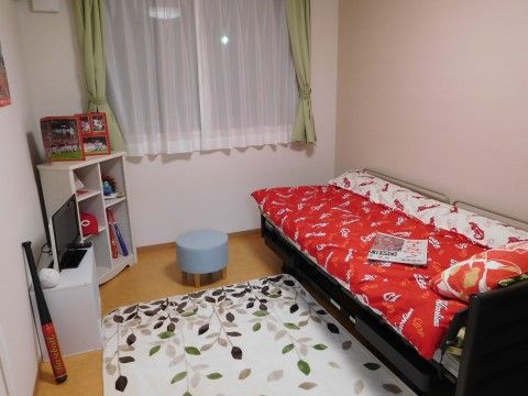 緑色のカーテンがつけられた部屋。白色の収納棚には入居者様の趣味用品が置かれており、自分好みの部屋にカスタマイズしている。