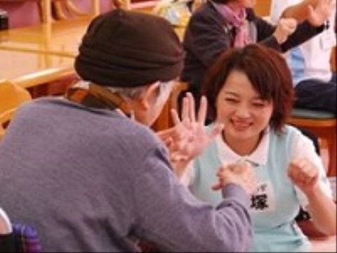 車椅子に座っている女性入居者と一緒に手遊びを楽しむ女性スタッフ
