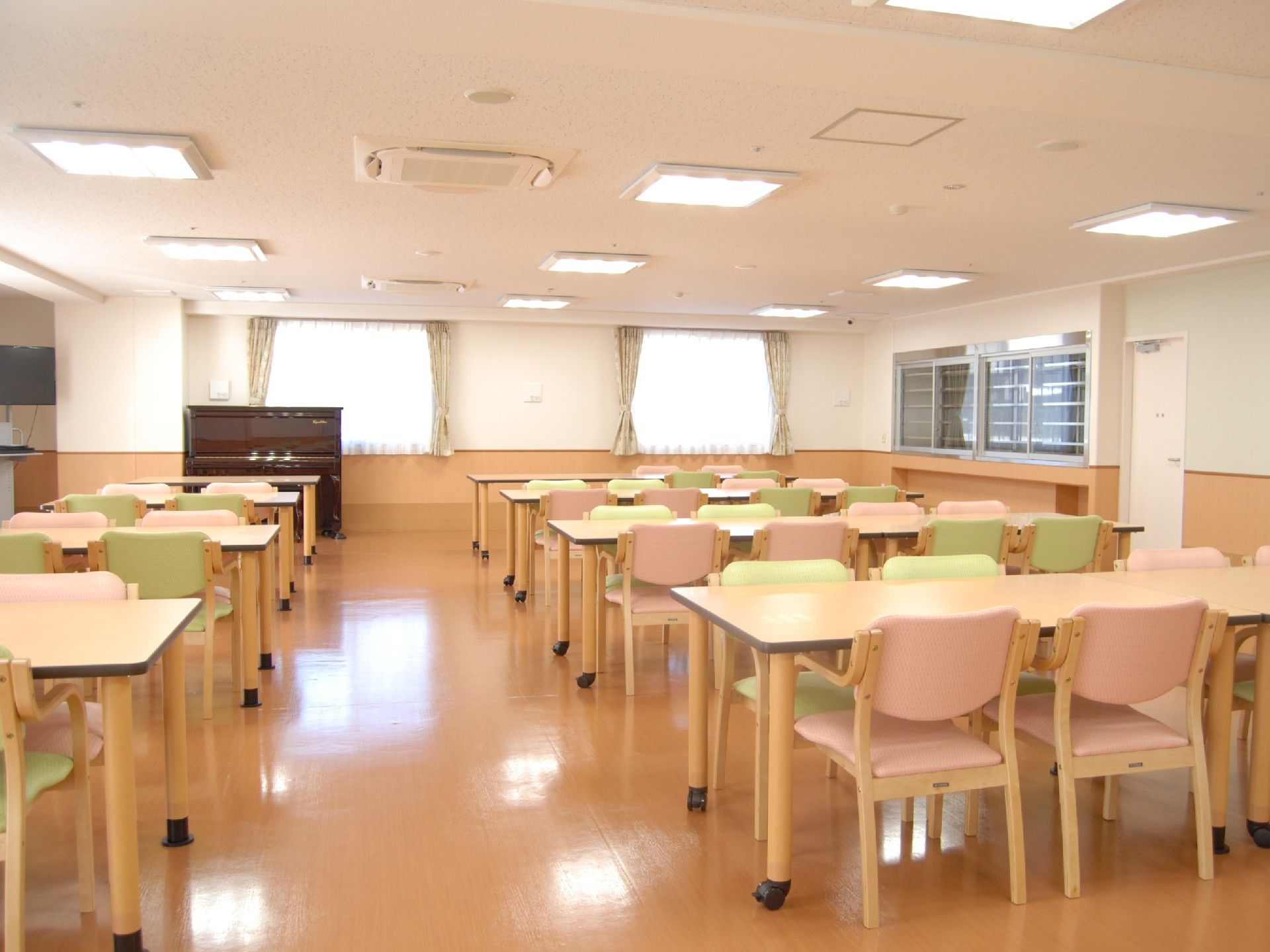 ピンクと薄緑の背もたれ椅子が設置されている、キャスター付きのテーブルが並んでいるダイニング