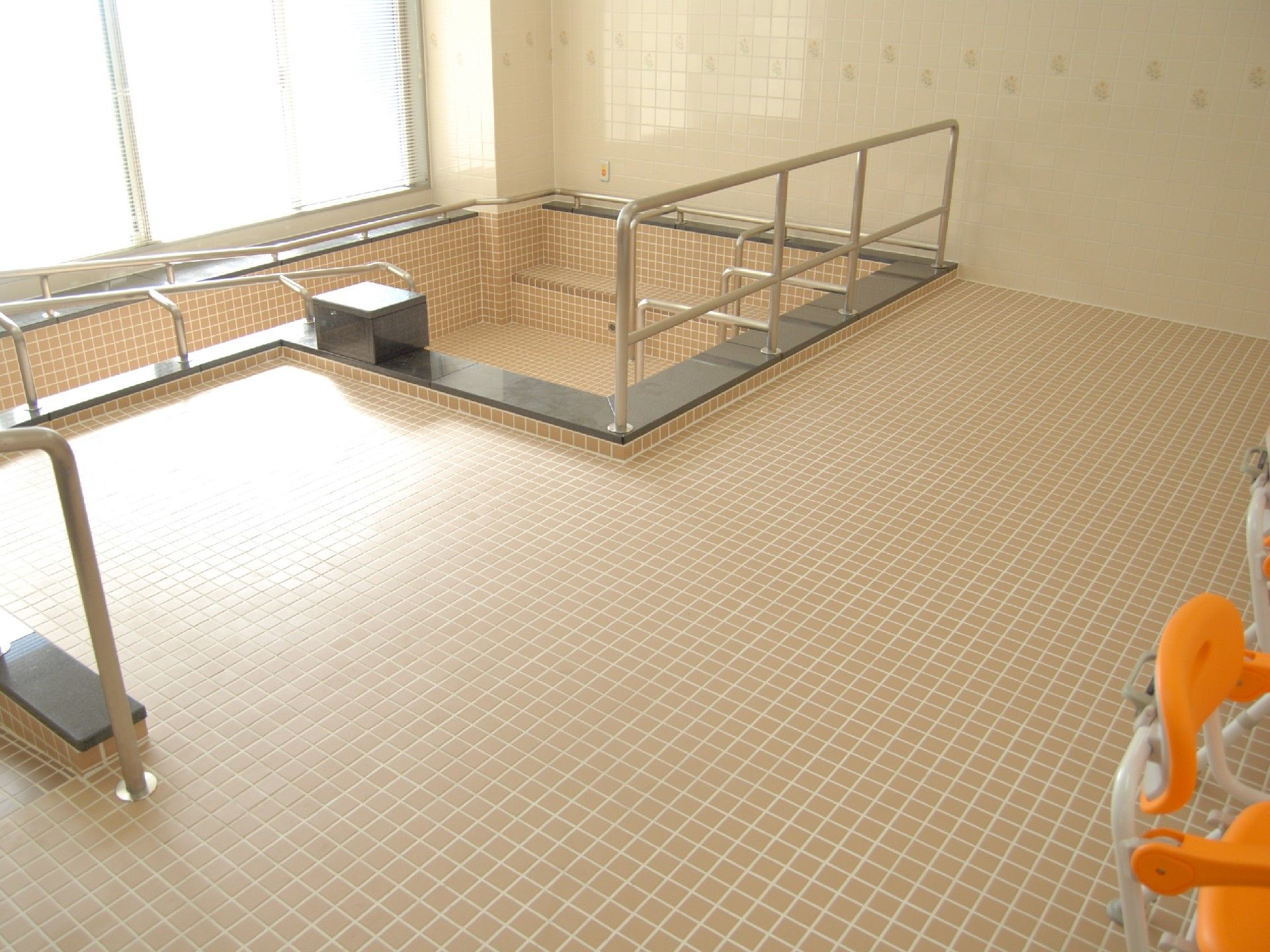 淡いピンク色のタイル張りの広々とした浴室である。大きな浴槽があり、スロープや手すりが設置されている。