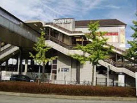 最寄り駅の駅前の様子である。屋根付きの歩道橋や階段を進むと駅舎に辿り着く。周囲は木々が植えられ整備されている。