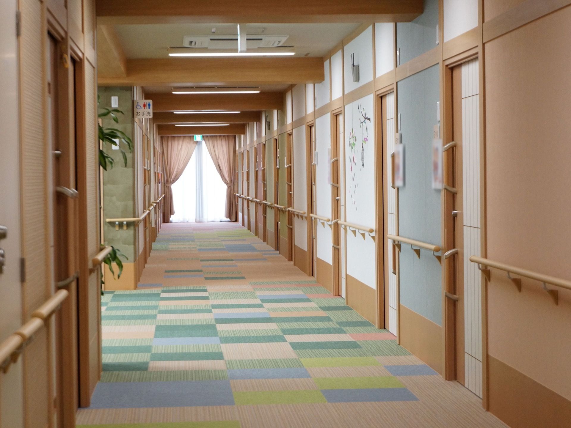 カラフルな床面の廊下。壁には絵が描かれている箇所がある。居室のドアは引き戸タイプで取っ手が上下に2箇所ついている。