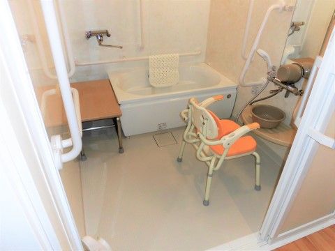 奥に白色の浴槽が設置され、手前にシャワーチェアが置かれている浴室