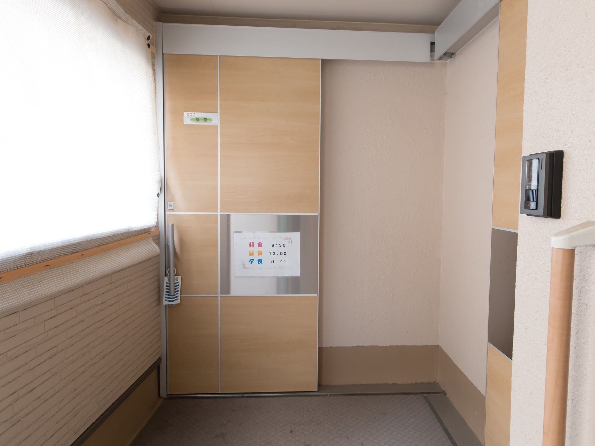 食堂の入口は吊り戸タイプの引き戸になっている。ドアの取っ手に虫よけがぶら下げられている。食事の時間が表示されている。