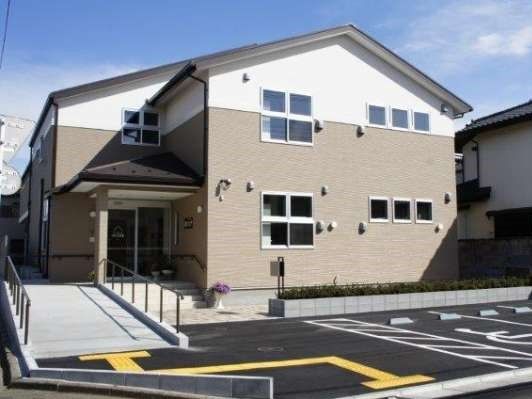 ２階建ての施設は、１階の端が玄関になっている。エントランス部分には滑らかな傾斜のスロープが設置され、建物の前は駐車場になっている。
