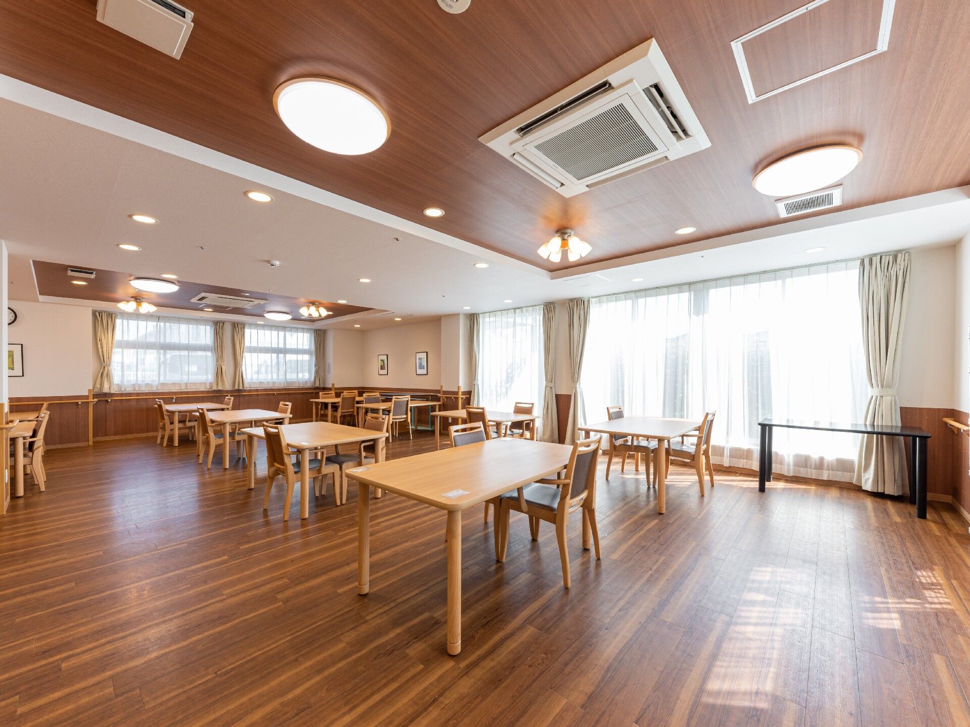 木と白色が基調の明るい食堂である。広々とした空間に、テーブルと椅子が並んでいる。調理室がすぐ近くに設置されている。