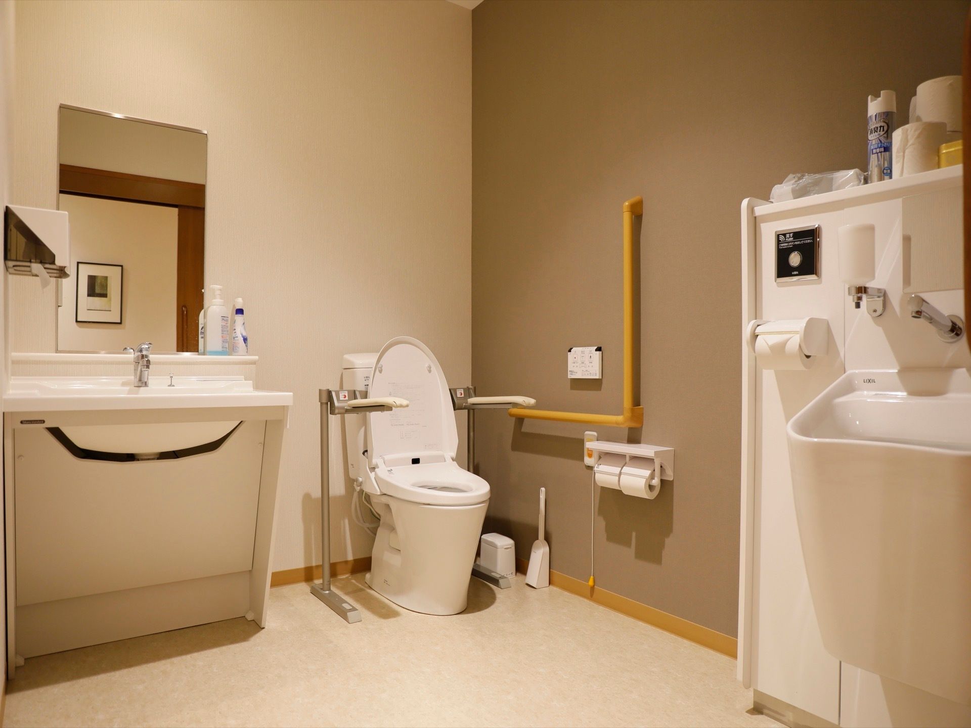 広いトイレには便器だけでなく、洗面台や鏡も設置されている。便座の近くには、手すりや水を流すためのボタン、ブザーなども付いている。