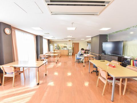 大きな窓にはピンクのカーテンがかかっており左側の壁はグレーになっている。テーブルが何台も置かれ、右側の壁にはテレビも用意されている。