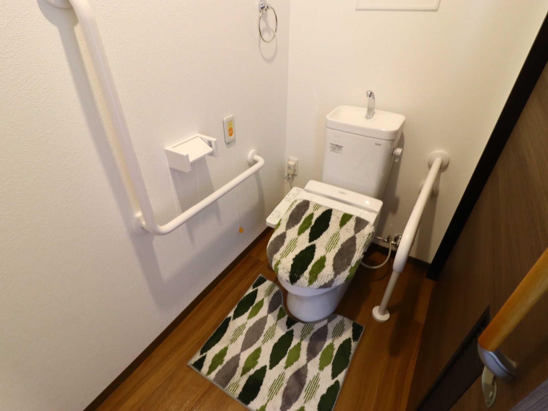 お部屋にはトイレが設けられているので、安心して過ごせる。壁と便器横には手すりが付いており、温水洗浄機能付き便座になっている。