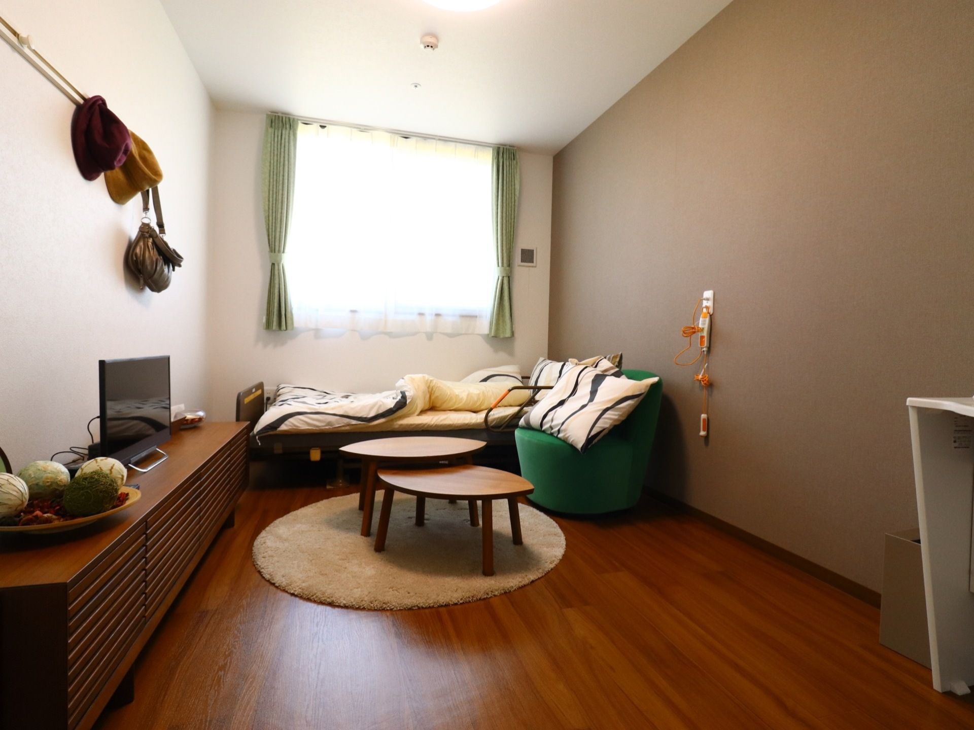お部屋は窓があり、木目調のフローリングになっている。ベッドやソファ、テレビ、テレビ台などがあり、今までと同じような生活ができる。
