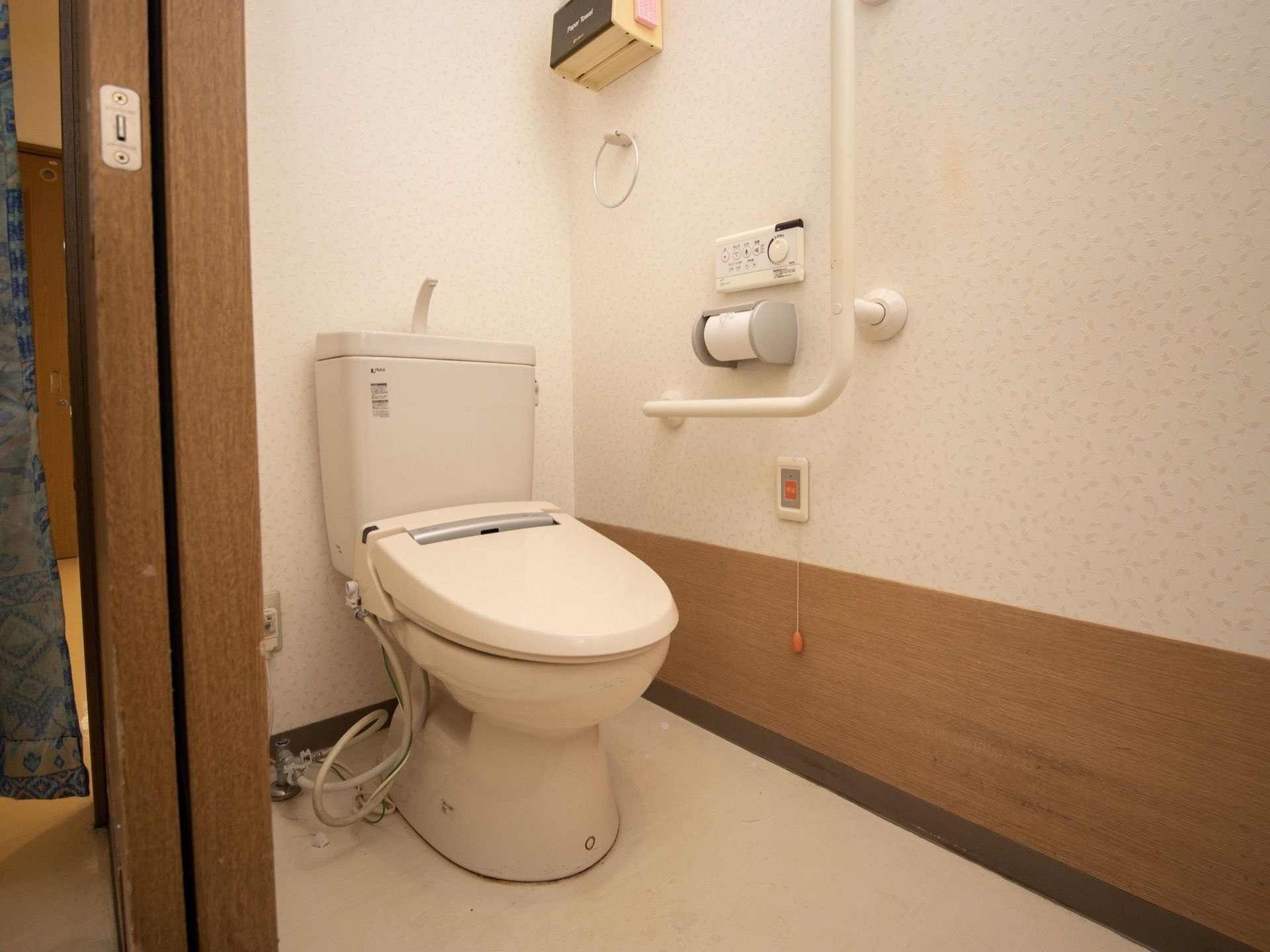 暖房便座付きトイレで、壁には手すりと呼び出しボタンが取りつけられている。トイレのドアは引き戸式になっている。