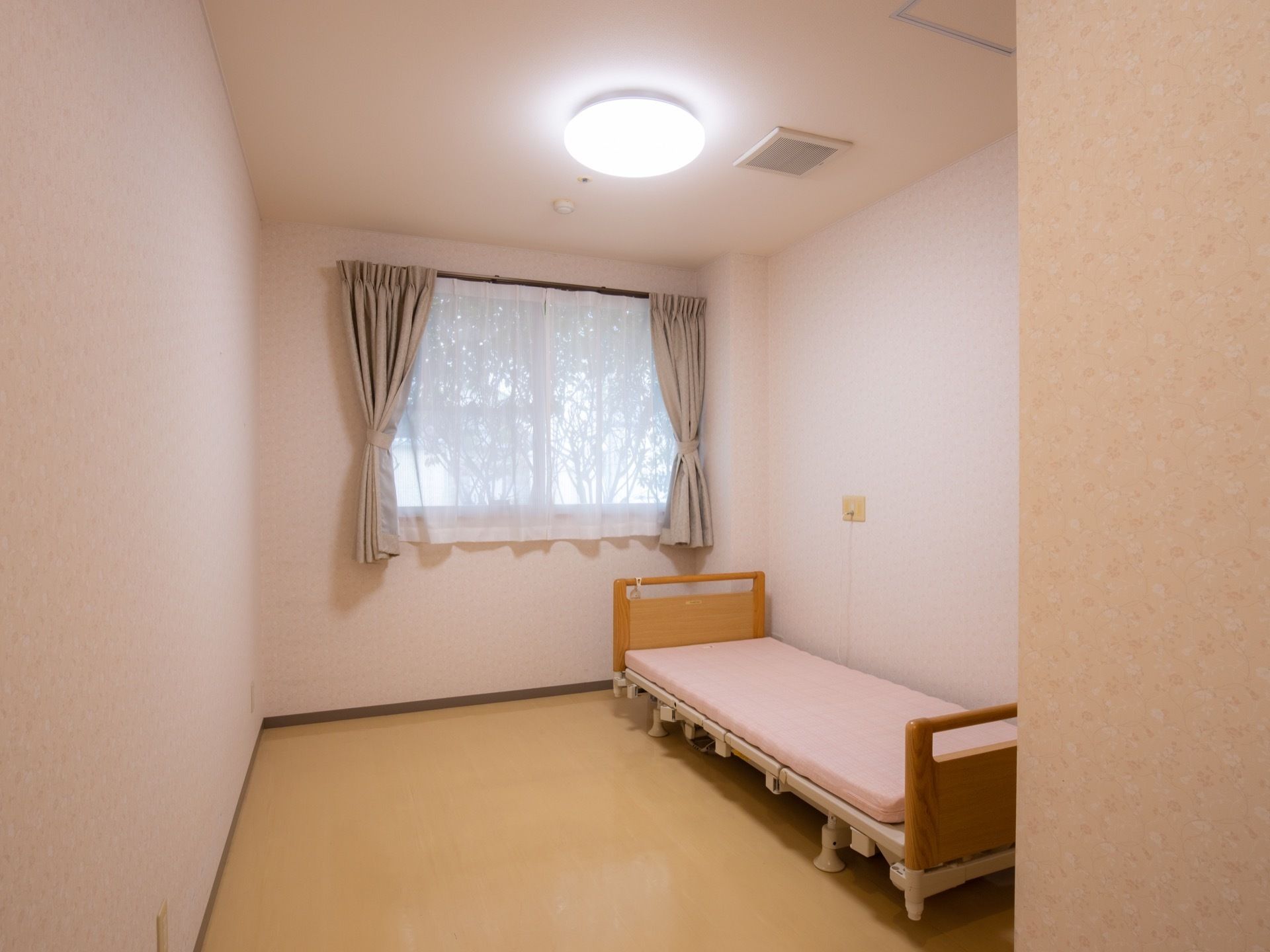 居室は程よい広さがあり、シングルベッドが用意されている。奥には、グレーのカーテンが掛けられた窓が設置されている。