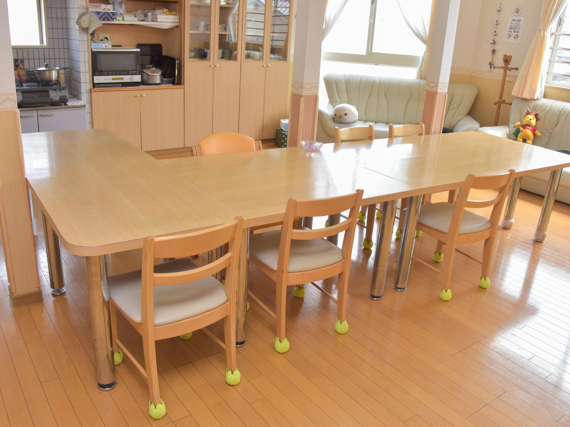 キッチンの前に並べられたテーブルセット。椅子には床を傷つけないよう、足に布がかぶせてある。窓の下にはソファが並んでいる。