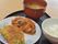 黒塗りのお盆の上に3つの食器が並んで写っている。ご飯と汁物と、2種類のおかずが彩りも豊かに盛られている。
