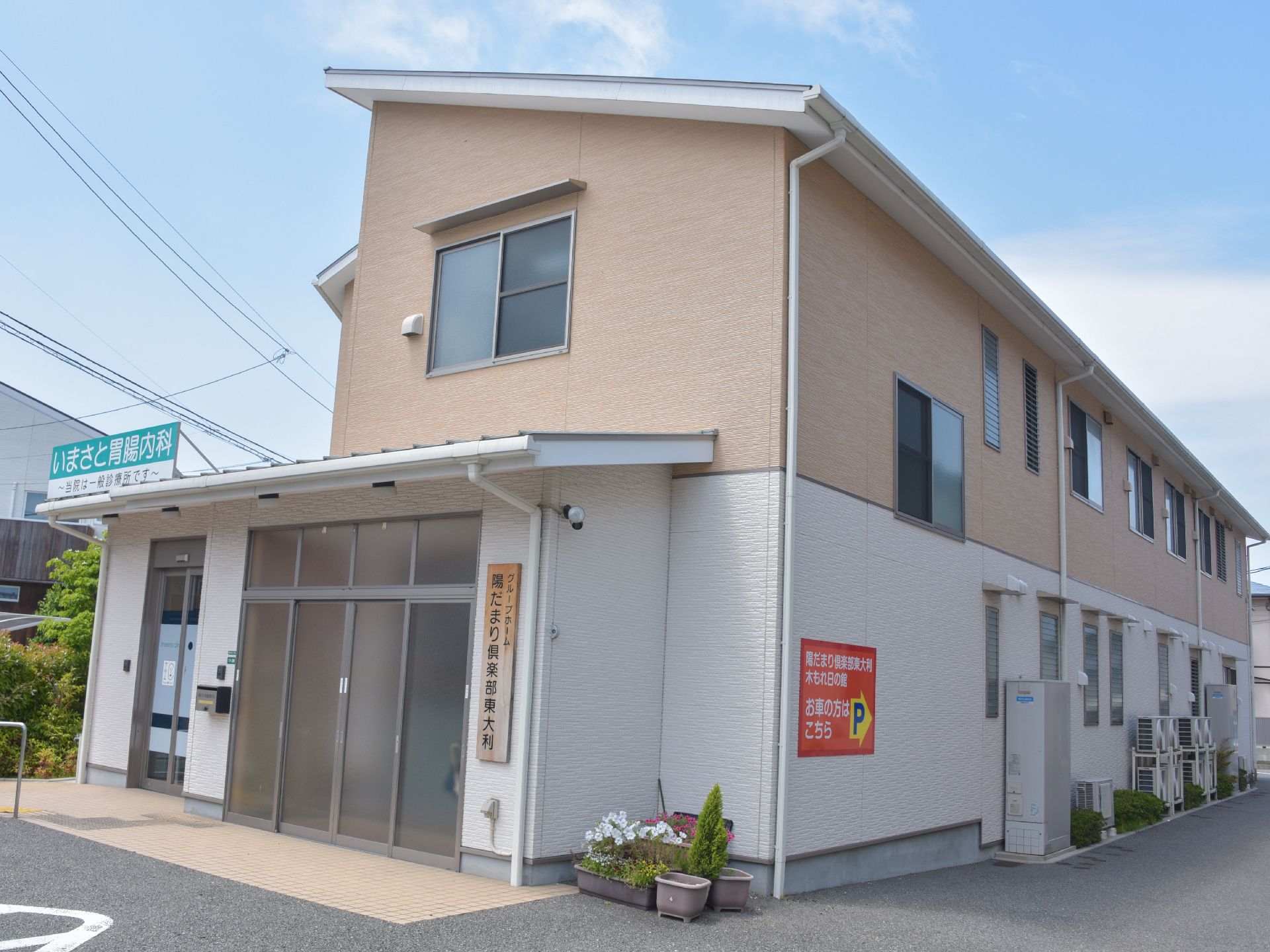 施設は2階建ての建物。手前には施設の看板と入り口の他にもう一つドアが並び、胃腸内科の看板が出ている。