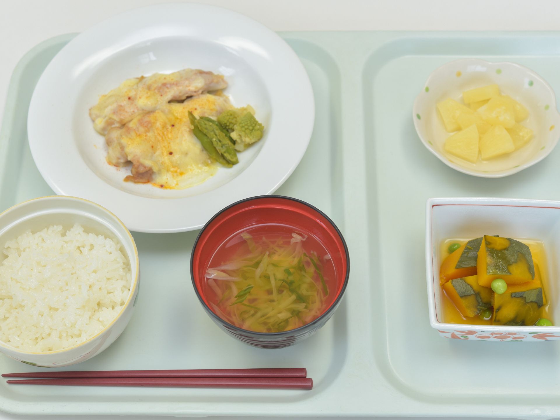 今日のメニューはご飯にお肉のチーズ焼き、かぼちゃの煮物、お吸い物、フルーツ。栄養のバランスが考えられていて、ボリュームもある。