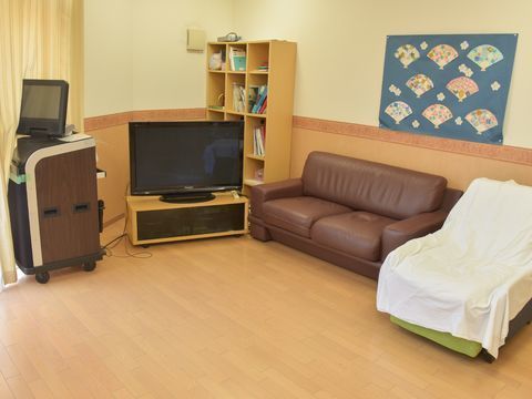 テレビの横に木製の棚や茶色のソファーが設置されている共有スペース