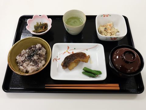 食事は和食が中心になっている。お赤飯と味噌汁、焼き魚にインゲンが添えられ、煮物やお茶などが配膳されているのが写されている。