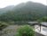 施設周辺は山々に囲まれており、リラックスできる環境となっている。山々の前には川も流れている。右側には白い建物がある。