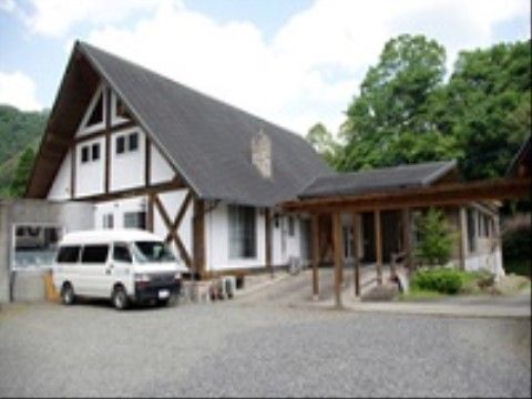 大きな黒い三角屋根の下に白い外壁が映える建物の前に、一台の車が停まっている様子