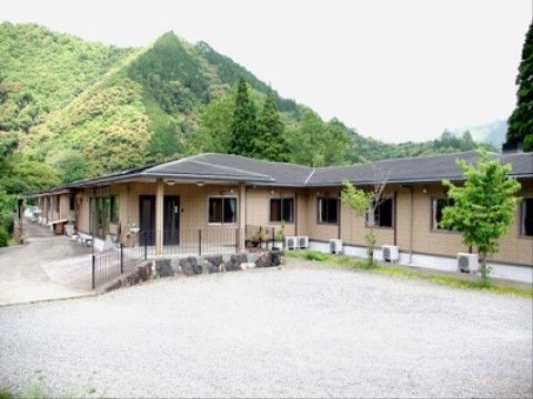 平屋建ての施設の後ろに、木々がたくさん植わっている山がある風景