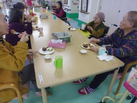 縦長のテーブルにつき、おやつタイムを楽しんでいる入居者
